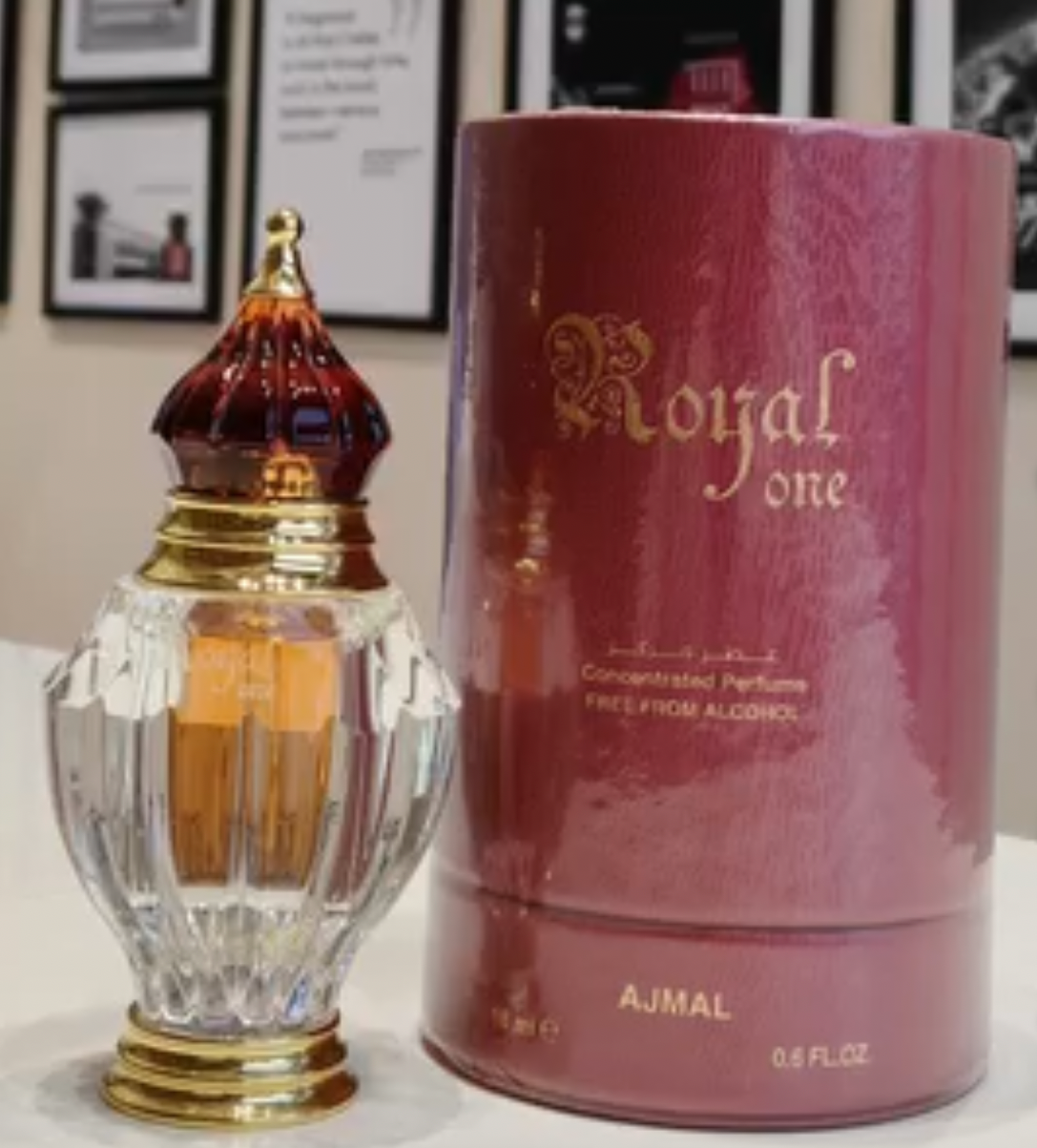 A bottle of Royal One attar and its pink cylindrical packaging box, displayed in front of a wall with framed black-and-white pictures.