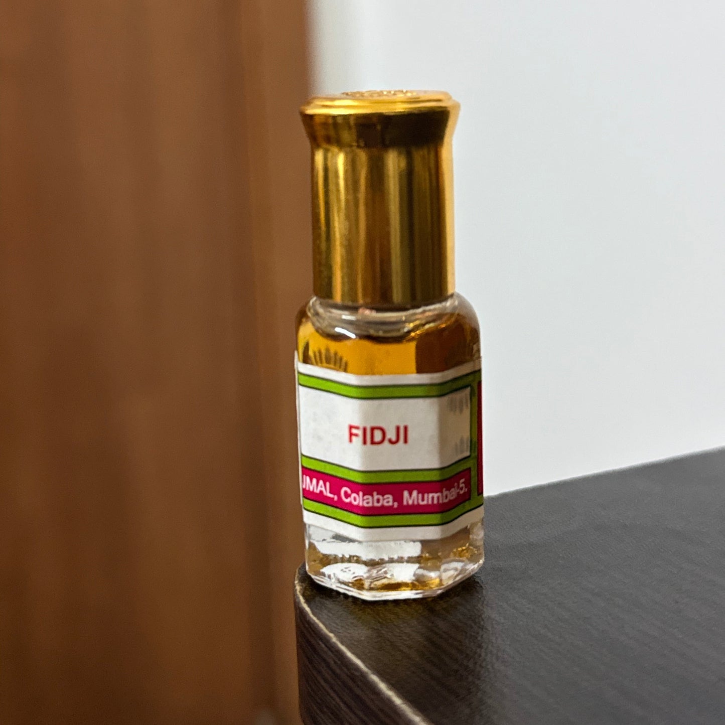 A small bottle of FIDJI perfume oil with a gold cap and a white label, resting on a dark wooden surface.