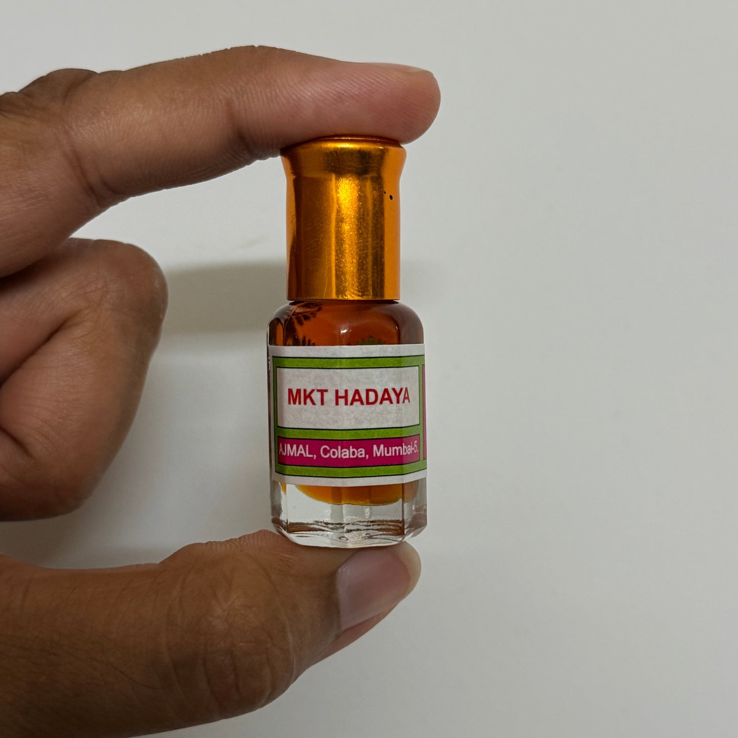 A hand holding a small glass bottle of MKT Hadaya perfume Oil against a plain light gray background.