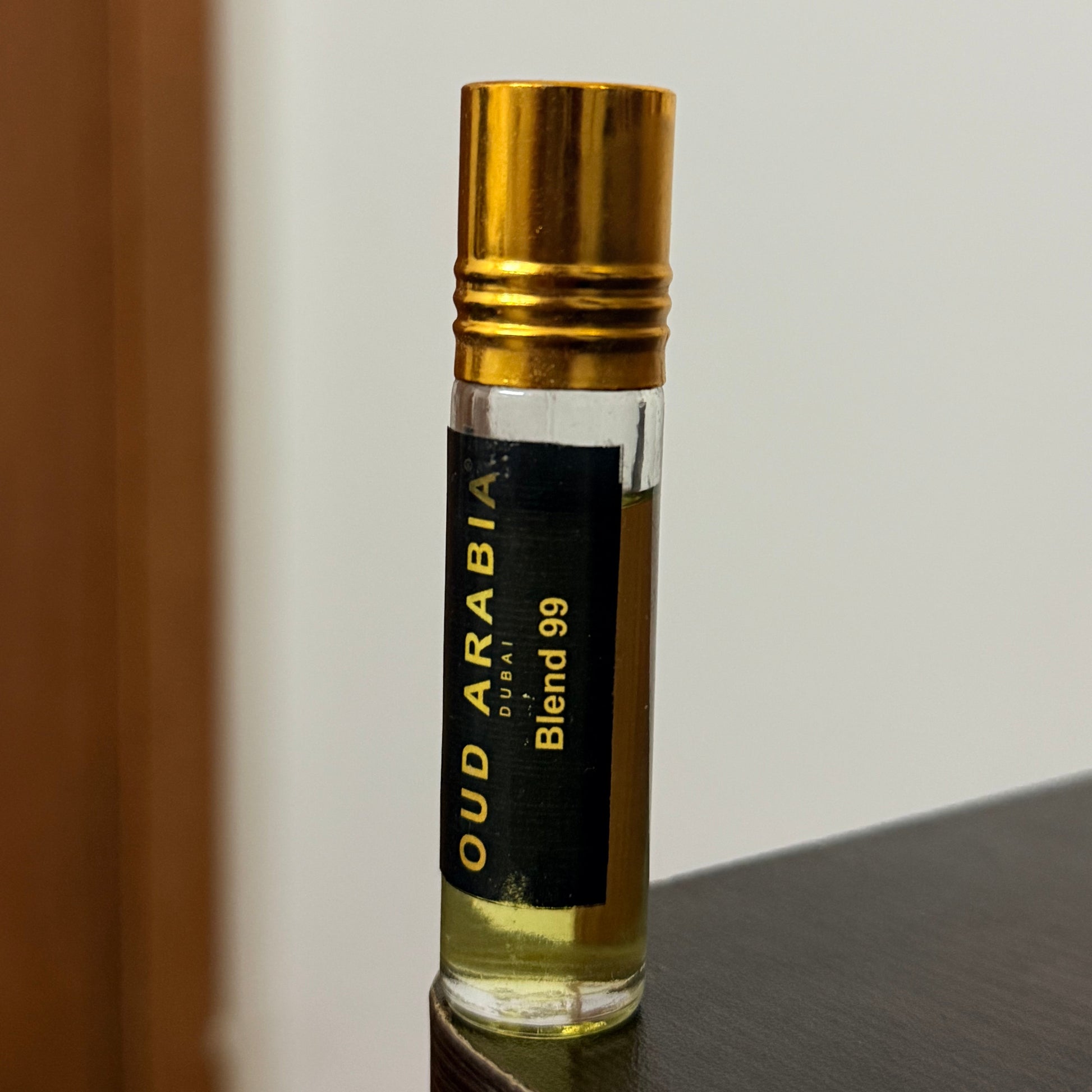 A small glass perfume vial with a gold cap and a black label reading 'OUD ARABIA Blend 99' and 'DEO', photographed against a plain light background.