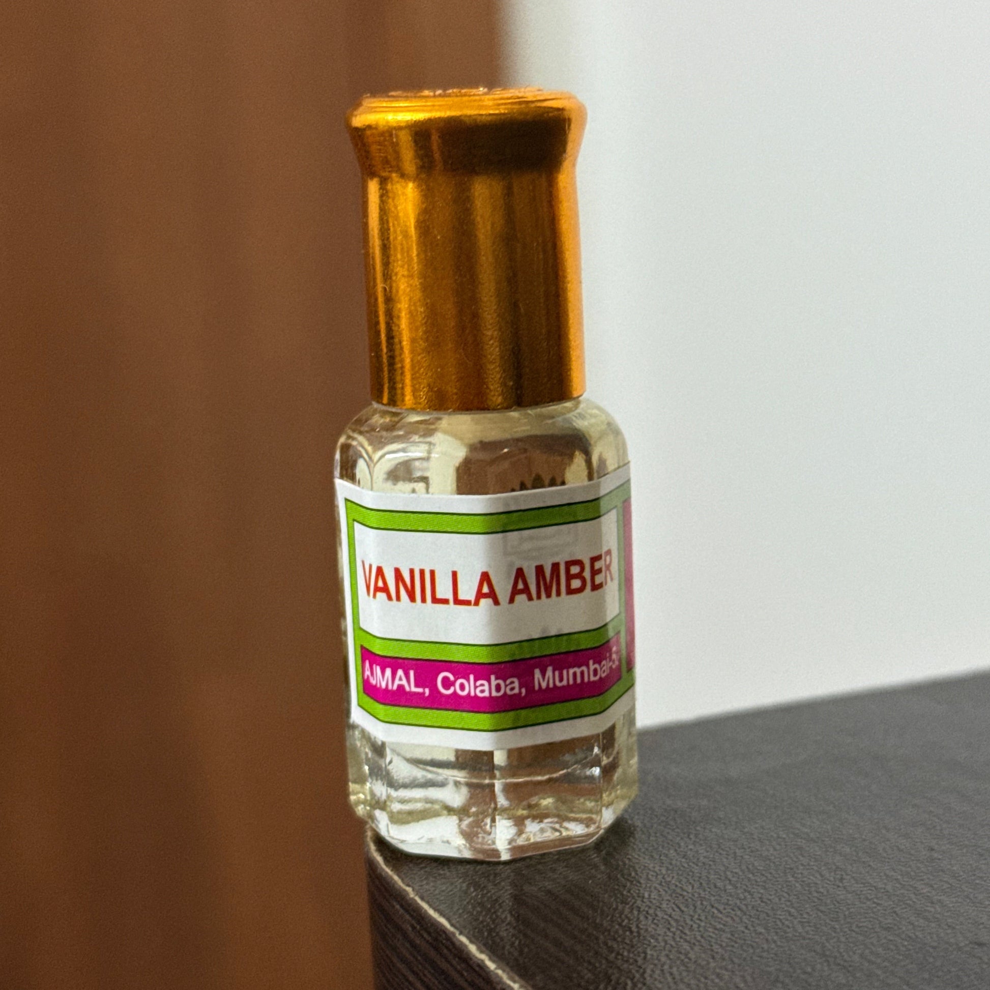 A small clear glass perfume bottle with a gold cap and a white label reading 'VANILLA AMBER'