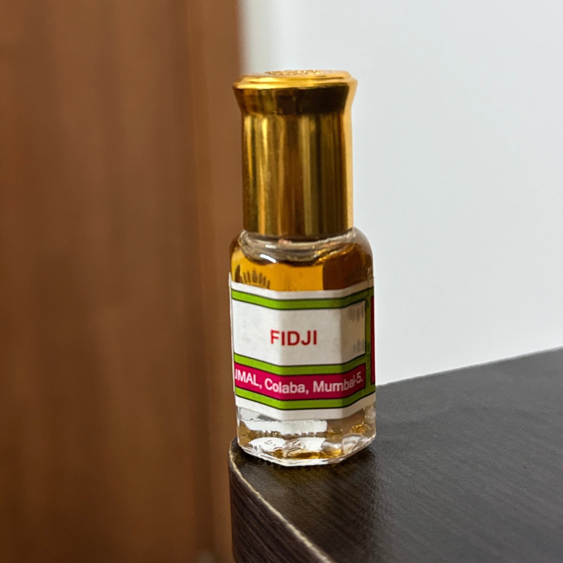 A small bottle of FIDJI perfume oil with a gold cap and a white label, resting on a dark wooden surface.