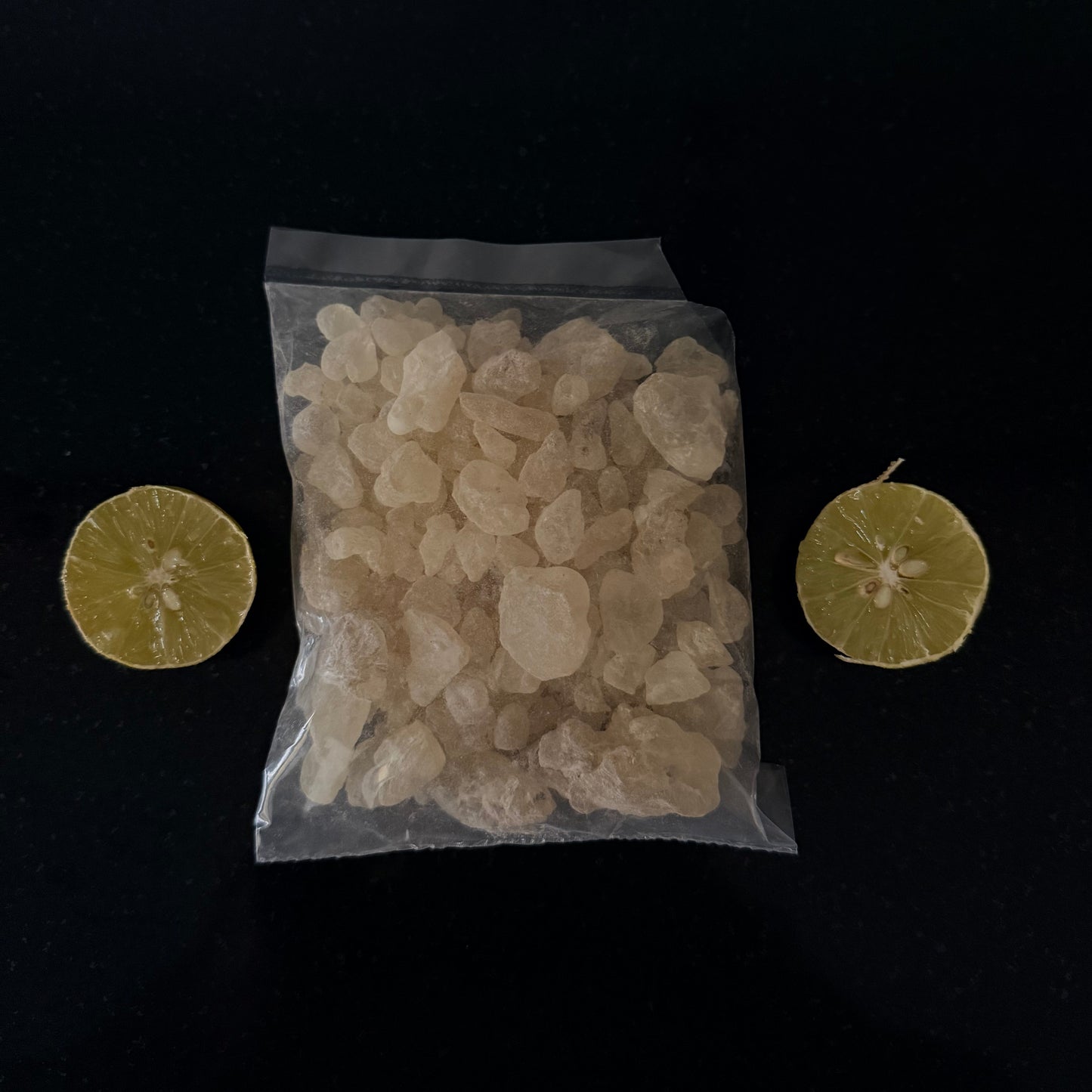 Clear bag of white hojari frankinsence with two lime slices on a black background