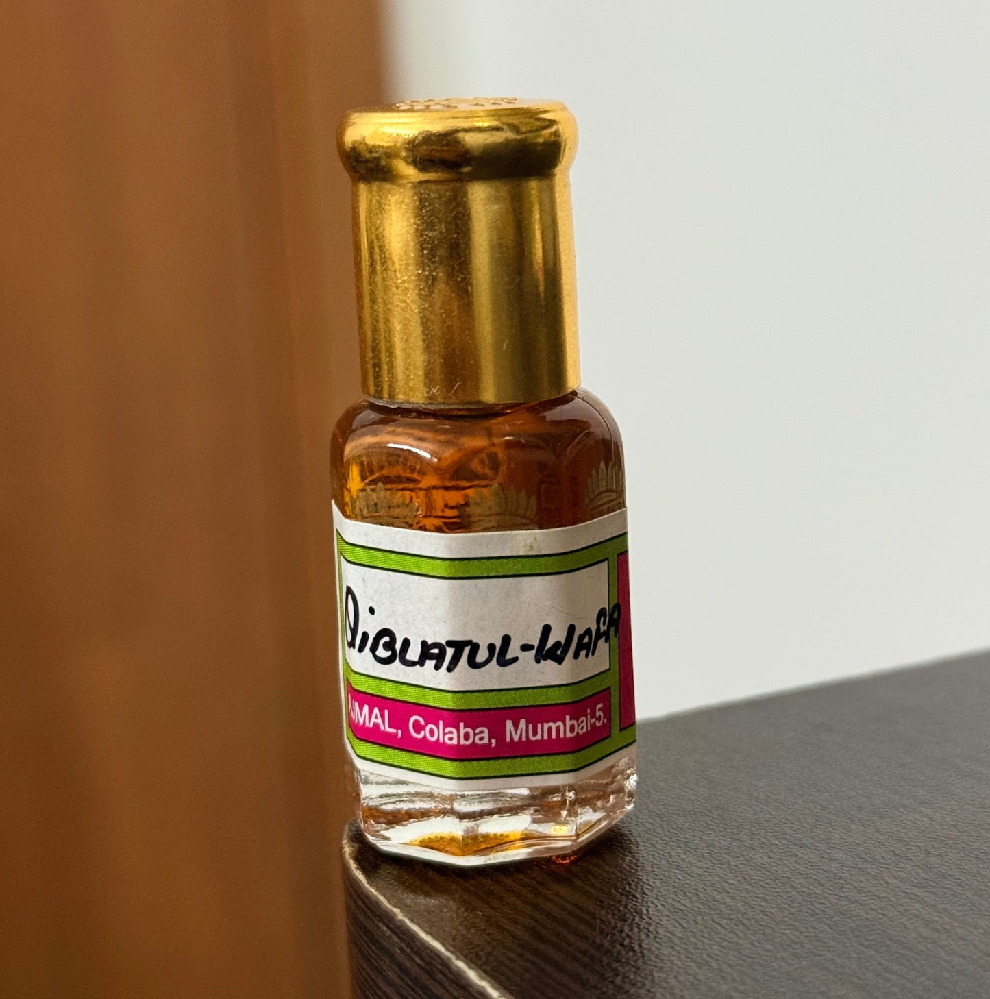 A small glass bottle of Thai peppermint oil with a gold cap and a white, green, and red label, resting on a dark wooden surface.